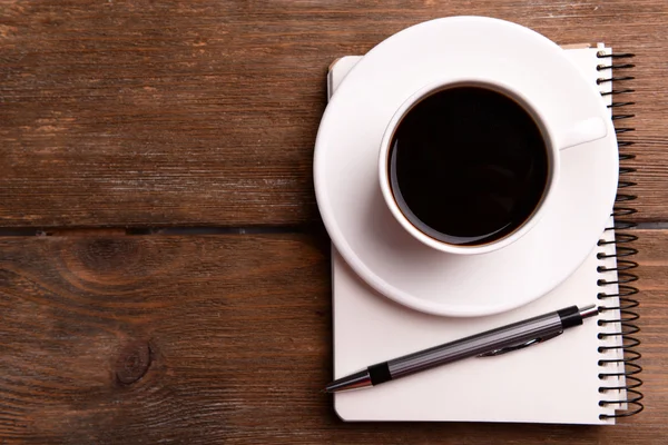 Xícara de café em pires com notebook e caneta sobre fundo de mesa de madeira — Fotografia de Stock