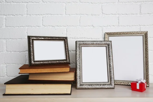 Gouden fotolijsten met boeken en huidige doos op houten oppervlak, op bakstenen muur achtergrond — Stockfoto