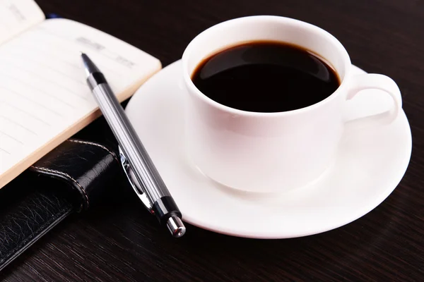 Xícara de café em pires com diário e caneta em fundo de mesa de madeira — Fotografia de Stock