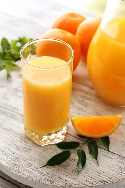 Glass of orange juice and oranges on color wooden table background — Stock Photo, Image