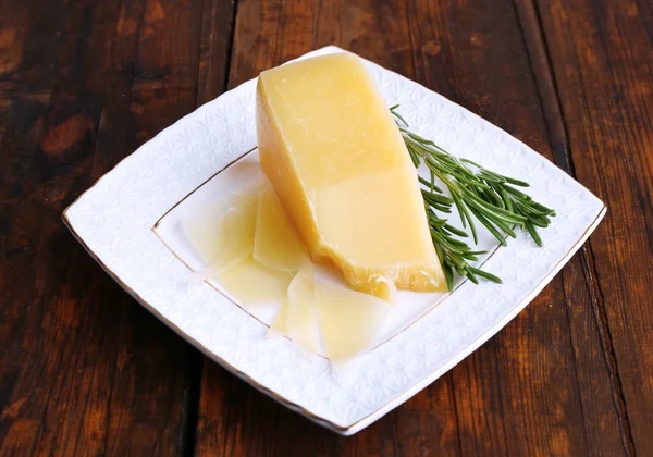 Parmesan cheese with sprig of rosemary on plate on wooden table background — Stock Photo, Image