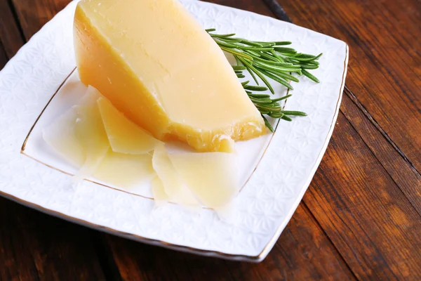 Parmesan cheese with sprig of rosemary on plate on wooden table background — Stock Photo, Image