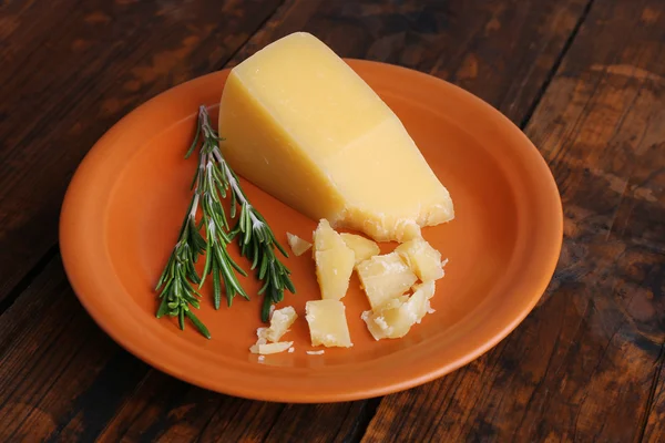 Parmesan cheese with sprig of rosemary on plate on wooden table background — Stock Photo, Image