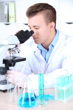 Erkek bilim adamı laboratuvarda mikroskop kullanıyor.