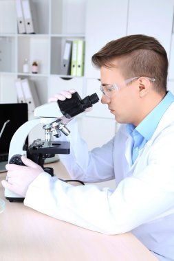 Erkek bilim adamı laboratuvarda mikroskop kullanıyor.