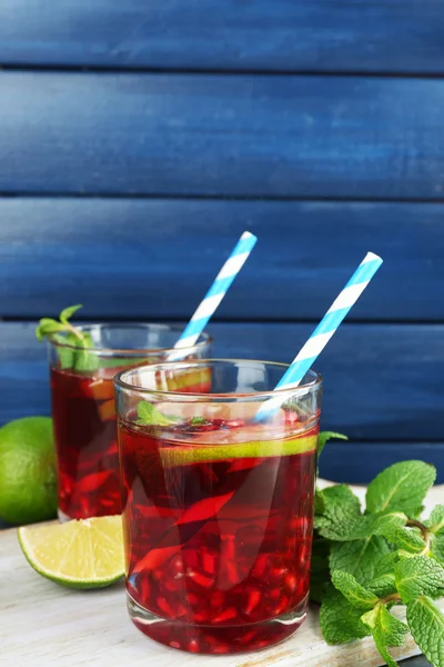 Bebida de granada en vasos con rodajas de lima y menta sobre fondo de madera de color — Foto de Stock