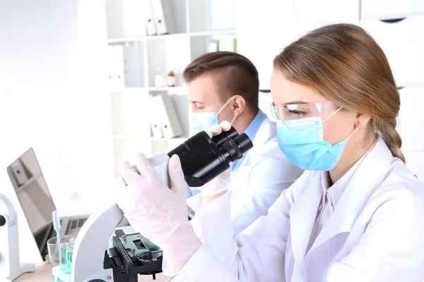 Científicas jóvenes y masculinas con microscopio en laboratorio —  Fotos de Stock