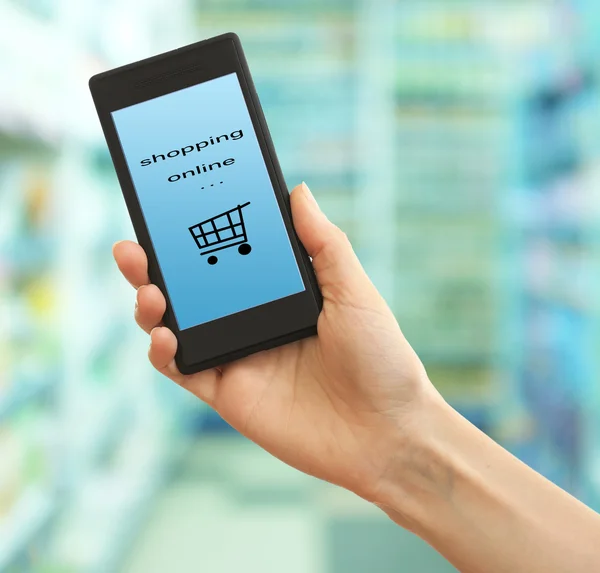 Mobile shopping concept. Hand holding mobile phone for internet shopping on supermarket background — Stock Photo, Image