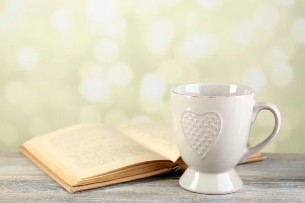 Cup of tea and book on table, on light background