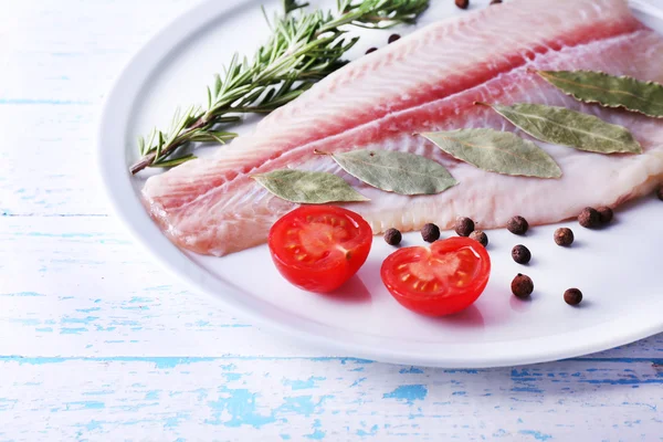 Pangasius fillet with herb and sliced cherry tomatoes on plate and color wooden table background — Stock Photo, Image