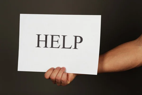 Sheet of paper with Help sign in male hand on dark background — Stock Photo, Image