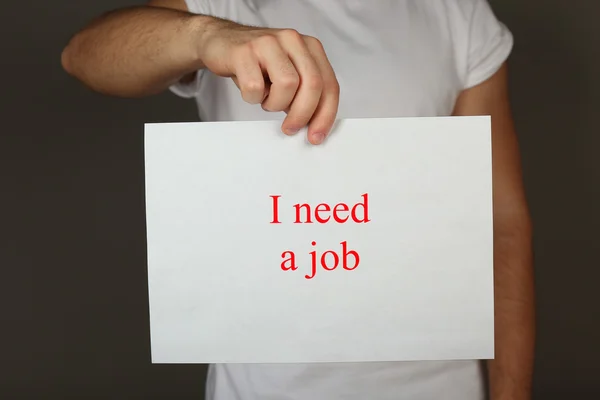 Sheet of paper with inscription I need a job in male hand on dark background — Stock Photo, Image