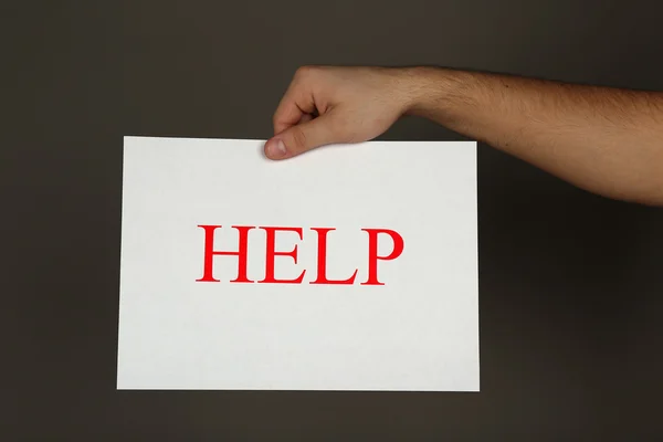 Sheet of paper with Help sign in male hand on dark background — Stock Photo, Image