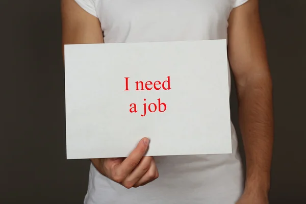 Sheet of paper with inscription I need a job in male hand on dark background — Stock Photo, Image