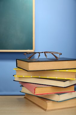 Ahşap masa, renkli duvar ve karatahta zemin üzerinde gözlüklü kitap yığını