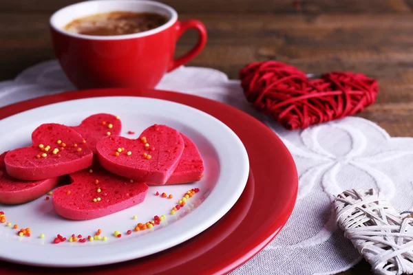 Cookies in form of heart in plate with cup of coffee on napkin, on rustic wooden planks background — Stock Photo, Image