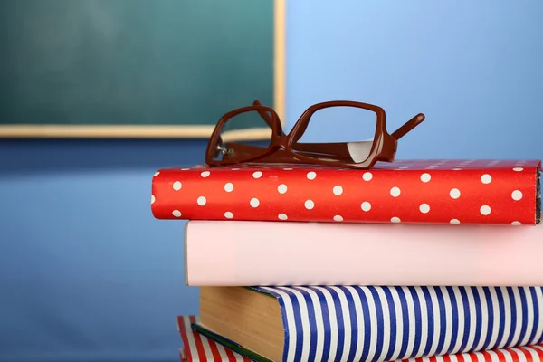 Stapel boeken met bril op houten bureau, op kleurrijke muur en schoolbord achtergrond — Stockfoto