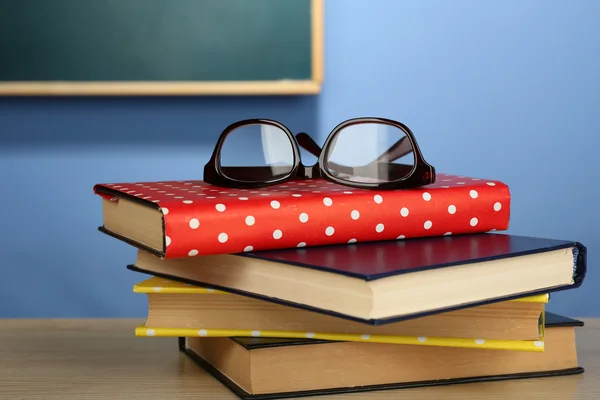 Pilha de livros com óculos na mesa de madeira, na parede colorida e no fundo do quadro negro — Fotografia de Stock