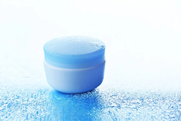 Cosmetische crème op blauwe achtergrond met water drops — Stockfoto