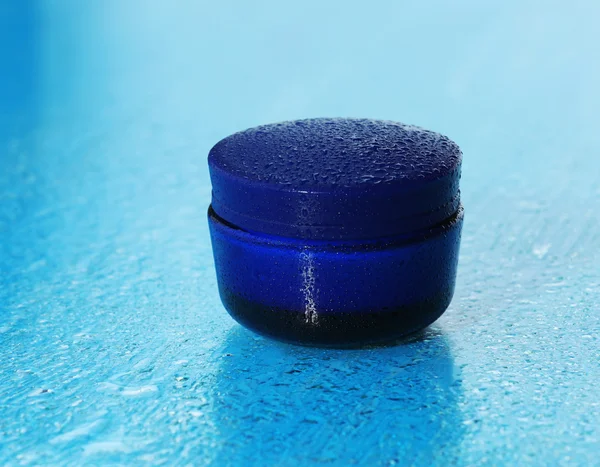 Kosmetisk kräm på blå bakgrund med vatten droppar — Stockfoto
