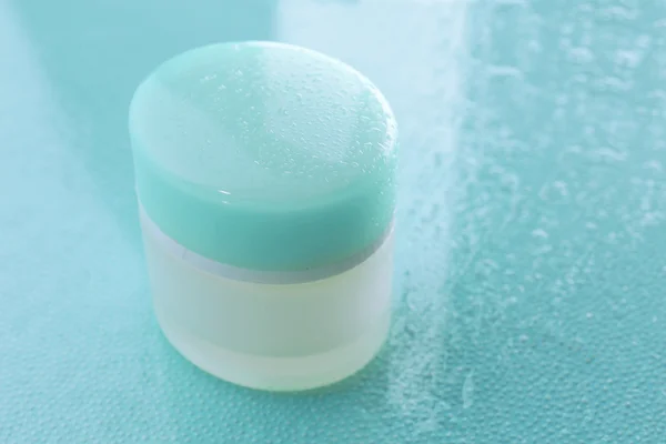 Kosmetikcreme auf blauem Hintergrund mit Wassertropfen — Stockfoto