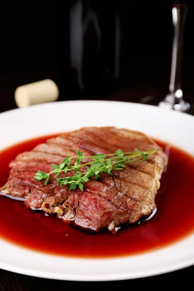 Gegrilde steak in wijnsaus met fles wijn op donkere achtergrond — Stockfoto
