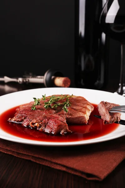 Grilled steak in wine sauce with glass of wine on dark background — Stock Photo, Image