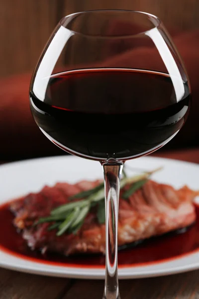 Grilled steak in wine sauce with glass of wine on wooden background