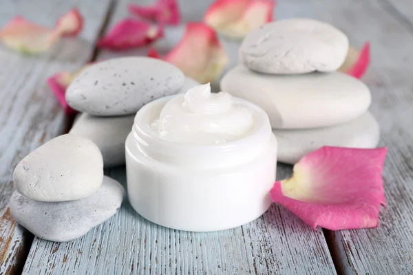 Cosmetische crème met rozenblaadjes en spa stenen op houten achtergrond — Stockfoto
