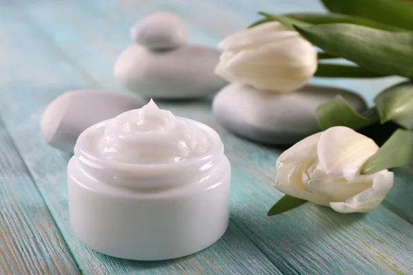 Crema cosmética con flores y piedras de spa sobre fondo de madera — Foto de Stock