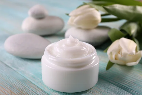 Crème cosmétique aux fleurs et pierres de spa sur fond de bois — Photo