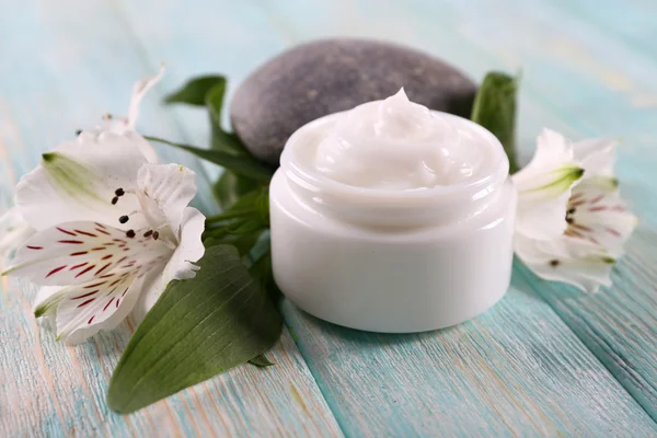 Crema cosmética con flores y piedras de spa sobre fondo de madera — Foto de Stock