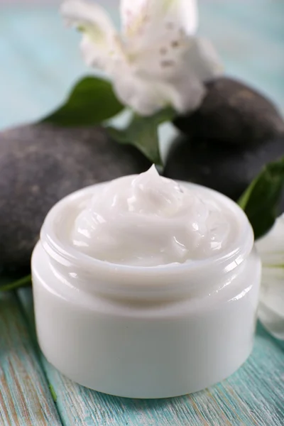 Crema cosmética con flores y piedras de spa sobre fondo de madera — Foto de Stock