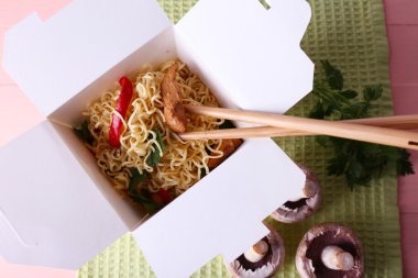 Çin eriştesi ve paket servisi olan restoran kutusunda pembe bir arka plan üzerinde yeşil peçete üzerinde sopa