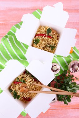 Çin eriştesi ve pembe bir arka plan üzerinde yeşil peçete paket servisi olan restoran kutularındaki sopa