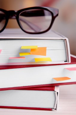 Books with bookmarks and glasses on table on bright background clipart