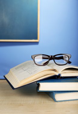 Ahşap masa, renkli duvar ve karatahta zemin üzerinde gözlüklü kitap yığını