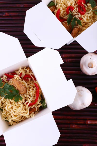 Chinese noodles in takeaway boxes on bamboo mat background — Stock Photo, Image