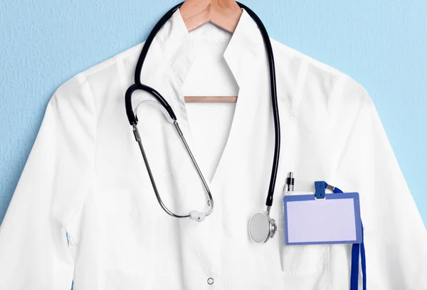 Doctor coat with stethoscope on hanger on blue background — Stock Photo, Image