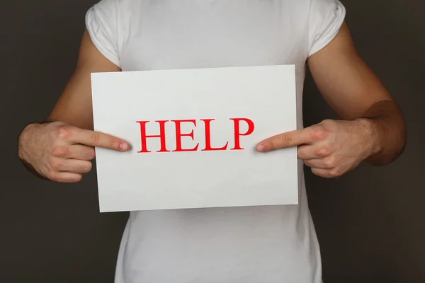 Sheet of paper with Help sign in male hands on dark background — Stock Photo, Image