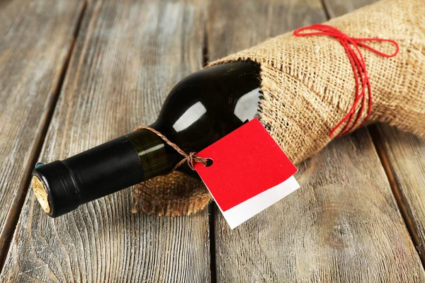 Bouteille de vin enveloppée dans un tissu de toile de jute sur des planches en bois — Photo