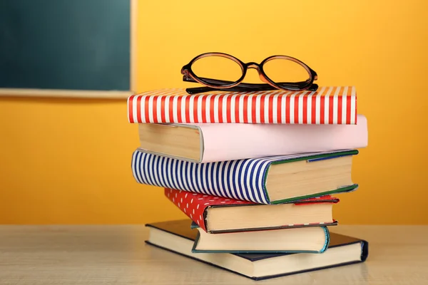 Montón de libros con gafas sobre escritorio de madera, sobre pared colorida y fondo de pizarra — Foto de Stock