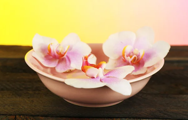 Ciotola con orchidee sul tavolo su sfondo luminoso — Foto Stock