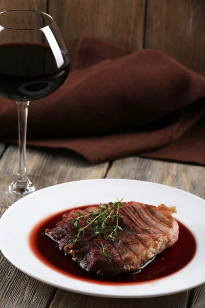 Bife grelhado em molho de vinho com copo de vinho em fundo de madeira — Fotografia de Stock