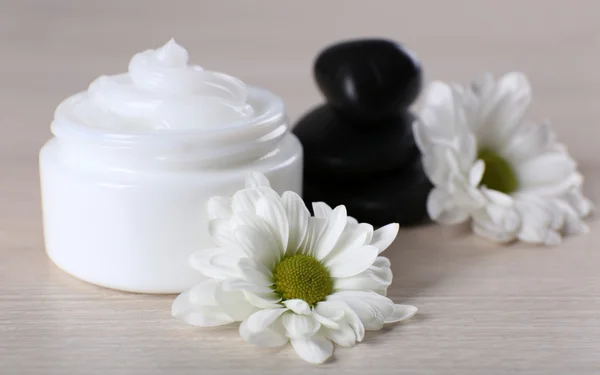 Crema cosmética con piedras de spa y flores sobre fondo de madera — Foto de Stock