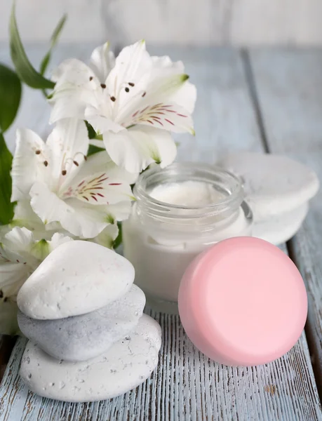 Kosmetikcreme mit Blumen und Wellness-Steinen auf Holzgrund — Stockfoto