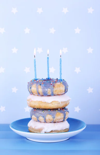 Délicieux beignets avec glaçage et bougies d'anniversaire sur la table sur fond lumineux — Photo