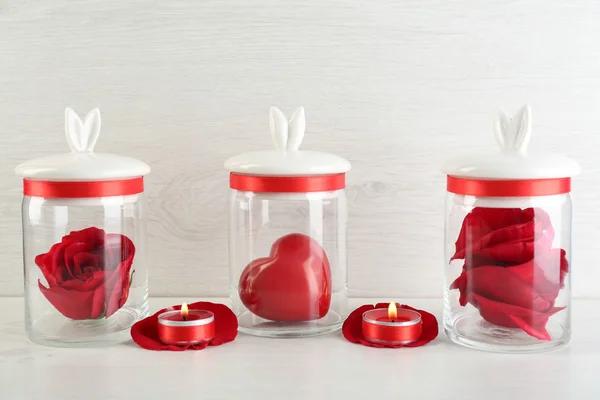 Rose flower, petals and decorative heart in glass jars on light background — Stock Photo, Image