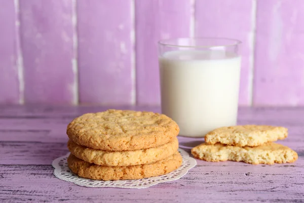 Biscotti saporiti e vetro di latte su sfondo di legno a colori — Foto Stock