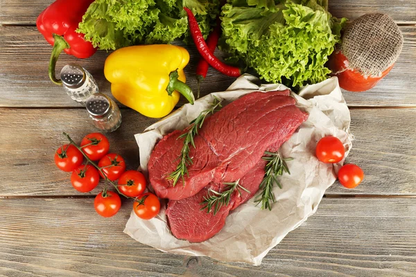 野菜と木の背景に緑の紙を生の牛肉ステーキ — ストック写真